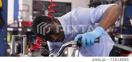 Afro american worker fixing failed motorcycle in workshop Afro american worker fixing failed motorcycle in workshop 72818880