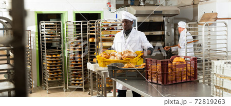 Positive african-american bakery worker lays fresh bread Positive african-american bakery worker lays fresh bread 72819263