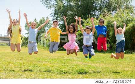 Happy school children jumping on the green lawn in park Happy school children jumping on the green lawn in park 72819674