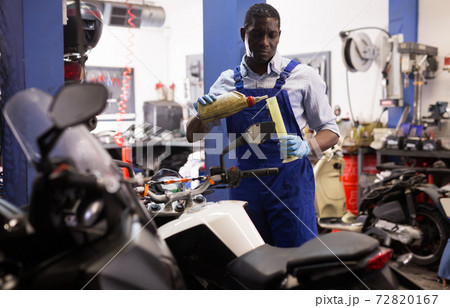 Engineer in overalls pours oil for motorcycle engine in garage 72820167