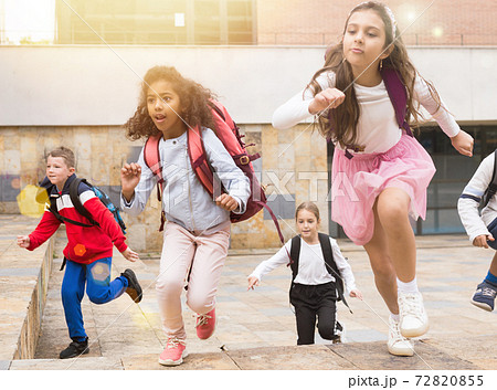 Tween boys and girls with school backpacks running in schoolyard 72820855