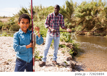 Man and boy holding fish on rod 72820894