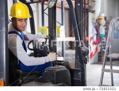 Hispanic worker of building materials warehouse driving forklift truck 72821321