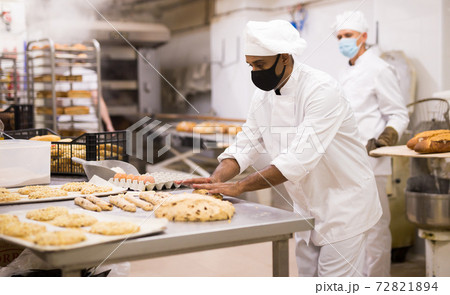 Baker at work in protective mask - making sweet buns with dough Baker at work in protective mask - making sweet buns with dough 72821894