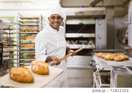 male baker with bread on baking shovel in kitchen male baker with bread on baking shovel in kitchen 72822103