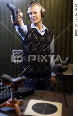 Man aiming smallbore sporting pistol at target in shooting range 72823632