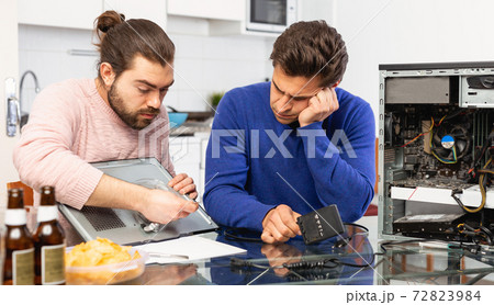 Two men repairing a desktop computer and drink beer 72823984