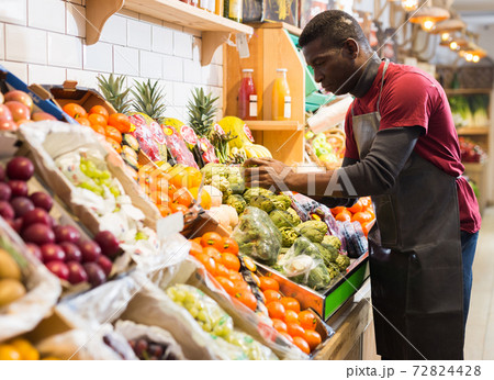 Salesman filling counter with vegetables and fruits Salesman filling counter with vegetables and fruits 72824428