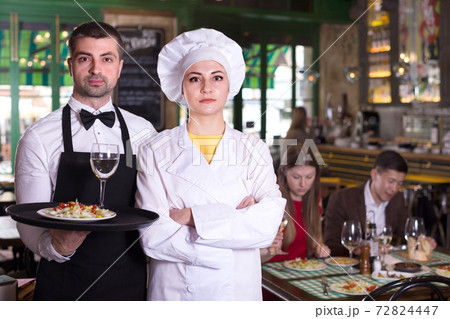 Man waiter and woman cook are standing with order for clients Man waiter and woman cook are standing with order for clients 72824447