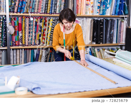 Female seller measuring and cutting off piece of textile 72825679
