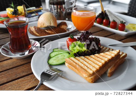 Triangular cut cheese toast in a plate with Turkish tea, fruit juice and breakfast table 72827344