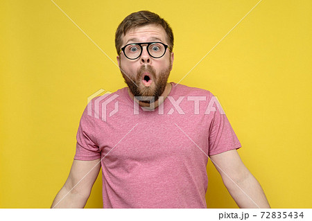 Man with glasses in shock, he opened mouth in surprise, looks with big eyes and spreads arms to the 72835434