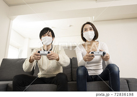 マスク姿で最新ビデオゲームを楽しむカップル/恋人同士でゲームを楽しむ姿/ゲーム機に夢中になる夫婦 72836198