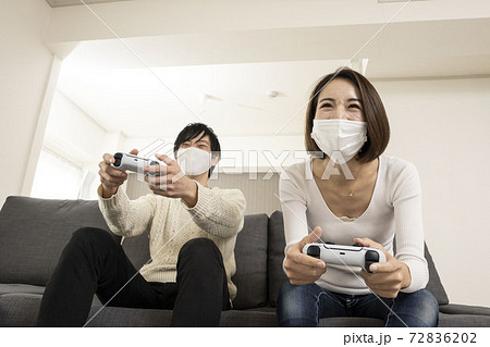 マスク姿で最新ビデオゲームを楽しむカップル 恋人同士でゲームを楽しむ姿 ゲーム機に夢中になる夫婦の写真素材 7262