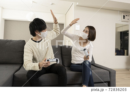 マスク姿で最新ビデオゲームを楽しむカップル 恋人同士でゲームを楽しむ姿 ゲーム機に夢中になる夫婦の写真素材 7263