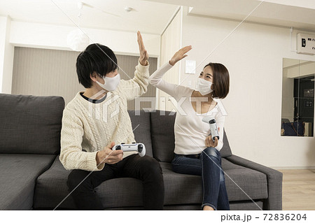 マスク姿で最新ビデオゲームを楽しむカップル/恋人同士でゲームを楽しむ姿/ゲーム機に夢中になる夫婦 72836204
