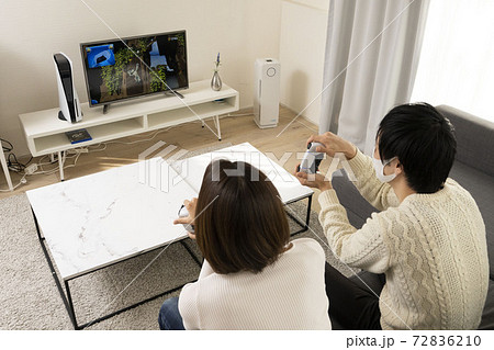 リビングでビデオゲームを楽しむカップル 恋人同士でゲームを楽しむ姿 ゲーム機に夢中になる夫婦の写真素材