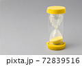 Yellow hourglass on gray paper background. 72839516