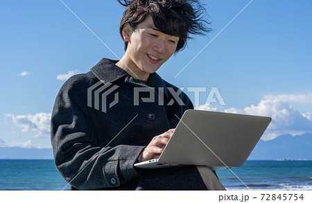 海辺でノートパソコンを使う男性 72845754