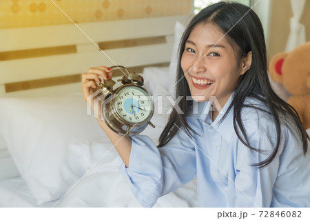 Beautiful young woman sitting on the bed holding alarm clock in hand. Beautiful young woman sitting on the bed holding alarm clock in hand. 72846082
