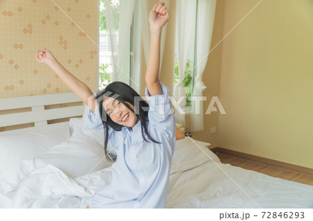 Asian beautiful girl wakes up, stretches her arms in a white bed in the bedroom. Asian beautiful girl wakes up, stretches her arms in a white bed in the bedroom. 72846293