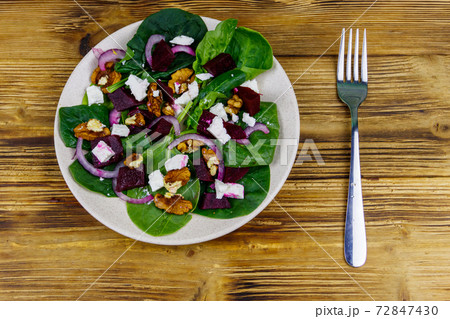 Tasty spinach salad with boiled beetroot, feta cheese, walnut and red onion on wooden table. Top view. Healthy vegetarian food Tasty spinach salad with boiled beetroot, feta cheese, walnut and red onion on wooden table. Top view. Healthy vegetarian food 72847430