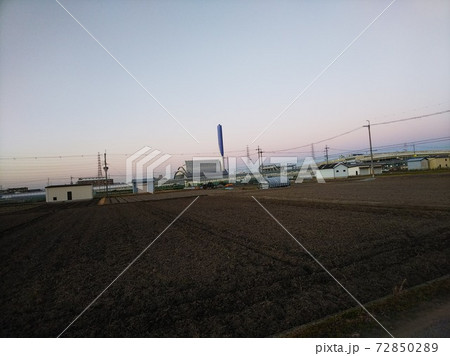 遠くに送電線が見える畑の風景、遠くに高速道路のジャンクション。背景にピンクに染まる夕暮れ空 72850289