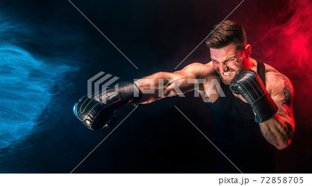 Bearded tattooed sportsman muay thai boxer in black undershirt and boxing gloves fighting on dark background with smoke. 72858705