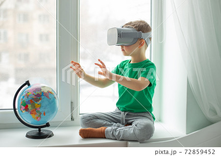A boy with a virtual reality headset is sitting at home at the table indoors. The child explores the world of virtual reality through video and games. A boy with a virtual reality headset is sitting at home at the table indoors. The child explores the world of virtual reality through video and games. 72859452