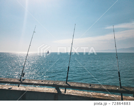 Fishing rods are waiting for biting on the pier. Against the background of sailing yachts. A warm summer day in California., USA 72864883