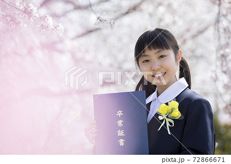 桜の前で卒業証書を持つ制服姿の女子小学6年生 卒業イメージの写真素材