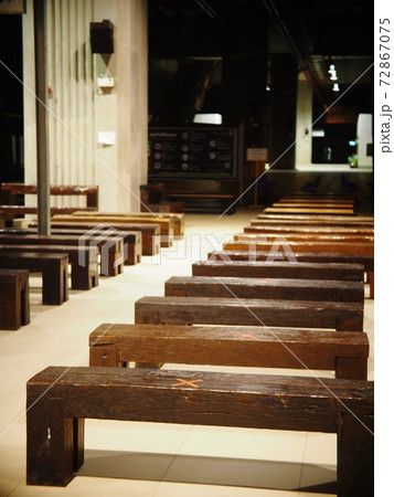blurred empty perspective view inside of railway train station at night with nobody focusing on red cross social distancing signs of the COVID-19 pandemic era on the wooden benches. 72867075
