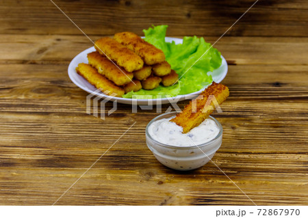 Fried fish fingers on a plate with lettuce and tartar sauce on wooden table Fried fish fingers on a plate with lettuce and tartar sauce on wooden table 72867970