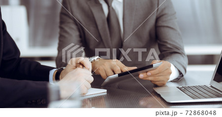 Unknown businessman using tablet computer and working together with his colleague while sits at the glass desk in modern office. Teamwork and partnership concept 72868048