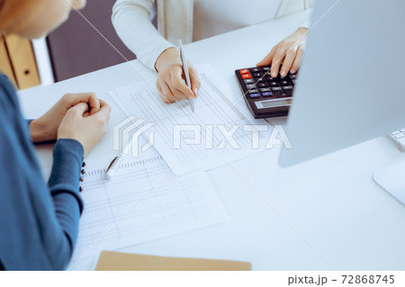 Accountant checking financial statement or counting by calculator income for tax form, hands close-up. Business woman sitting and working with colleague at the desk in office. Audit concept Accountant checking financial statement or counting by calculator income for tax form, hands close-up. Business woman sitting and working with colleague at the desk in office. Audit concept 72868745