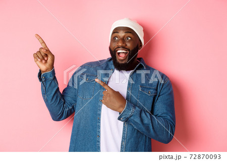 Amazed Black guy showing awesome promo offer, smiling and pointing fingers at upper left corner banner, pink background Amazed Black guy showing awesome promo offer, smiling and pointing fingers at upper left corner banner, pink background 72870093
