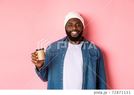 Handsome modern Black man drinking takeaway coffee, smiling and looking satisfied at camera, standing over pink background Handsome modern Black man drinking takeaway coffee, smiling and looking satisfied at camera, standing over pink background 72871131