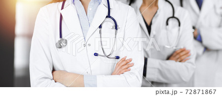 Group of professional doctors is standing as a team with arms crossed in sunny clinic. Medicine concept during Coronavirus pandemic. Covid-2019 72871867