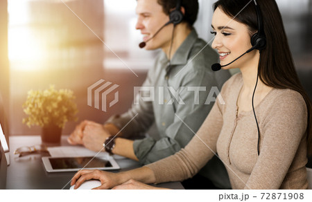 Call center operators at work. Two young people in headsets are talking to the clients, while sitting in sunny office 72871908