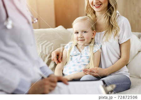 Doctor and patient in sunny room. Pediatrician using clipboard while examining little girl with her mother at home. Medicine concept 72872506