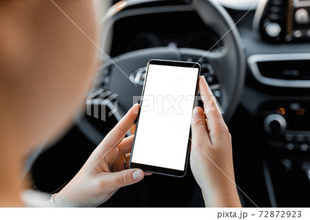 Young driver using smartphon in the car while driving or parking. Mockup of a mobile phone with isolated white screen in the hands of a woman. 72872923