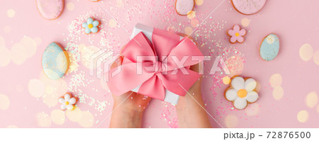 Colorful easter cookies with icing and gifr box in kid hands on pink background, colorful seasonal holiday concept, stylish greeting card, invitation, flyer. copy space, banner 72876500