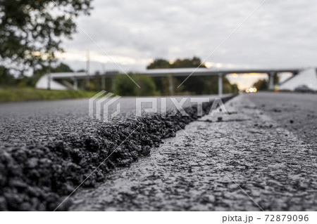 A large layer of fresh hot asphalt. Layer of asphalt raw material in a shallow depth of field. Rollers rollin fresh hot asphalt on the new road. Road construction. Construction of a new road. 72879096