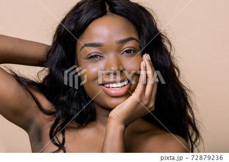 Attractive smiling African American lady with perfect skin and nude makeup, keeping one hand under chin and another behind head, posing at camera on beige background. Natural beauty Attractive smiling African American lady with perfect skin and nude makeup, keeping one hand under chin and another behind head, posing at camera on beige background. Natural beauty 72879236