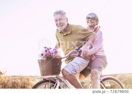 Cheerful mature couple of senior enjoy the outdoor leisure activity together riding a bike and laughing a lot - happy elderly active lifestyle with caucasian old people having fun 72879600