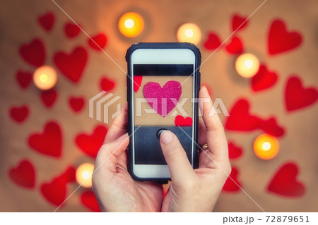 Female hands holding mobile phone taking a photo of pink romantic Valentine's hearts . Greeting card for Valentines Day top view, romantic background Female hands holding mobile phone taking a photo of pink romantic Valentine's hearts . Greeting card for Valentines Day top view, romantic background 72879651