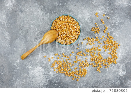 Uncooked corn kernels in blue bowl with wooden spoon 72880302