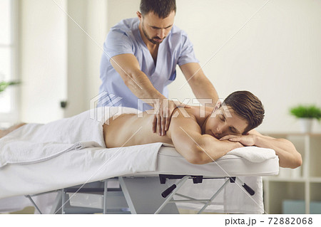 Young man getting relaxing body massage done by professional masseur in spa salon 72882068