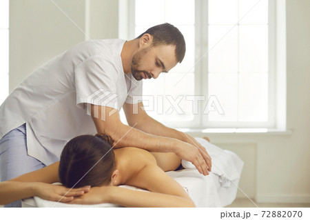 Professional massagist doing back massage for young woman lying on massage table Professional massagist doing back massage for young woman lying on massage table 72882070