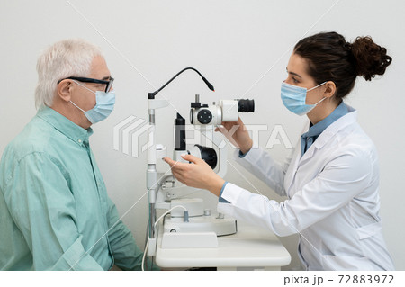 Side view of young female ophthalmologist using medical equipment in clinics Side view of young female ophthalmologist using medical equipment in clinics 72883972
